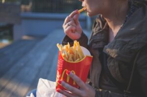 Na foto: Mulher comendo fritas, uma fast food.